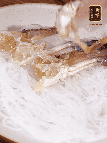 盤底墊上粉絲，擺上梭子蟹、火腿片，撒姜粒，淋上蒸魚豉油、花雕酒調(diào)味腌制15分鐘